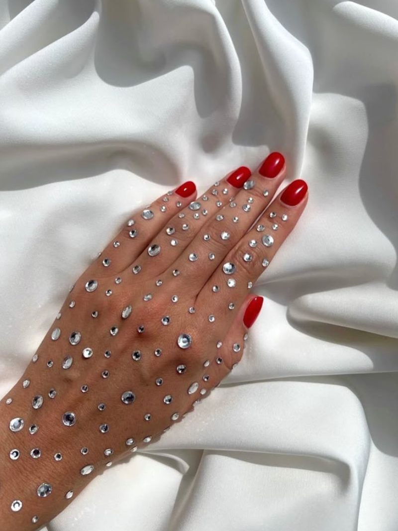Une main aux ongles rouges ornée de strass, sur un drapé de satin blanc